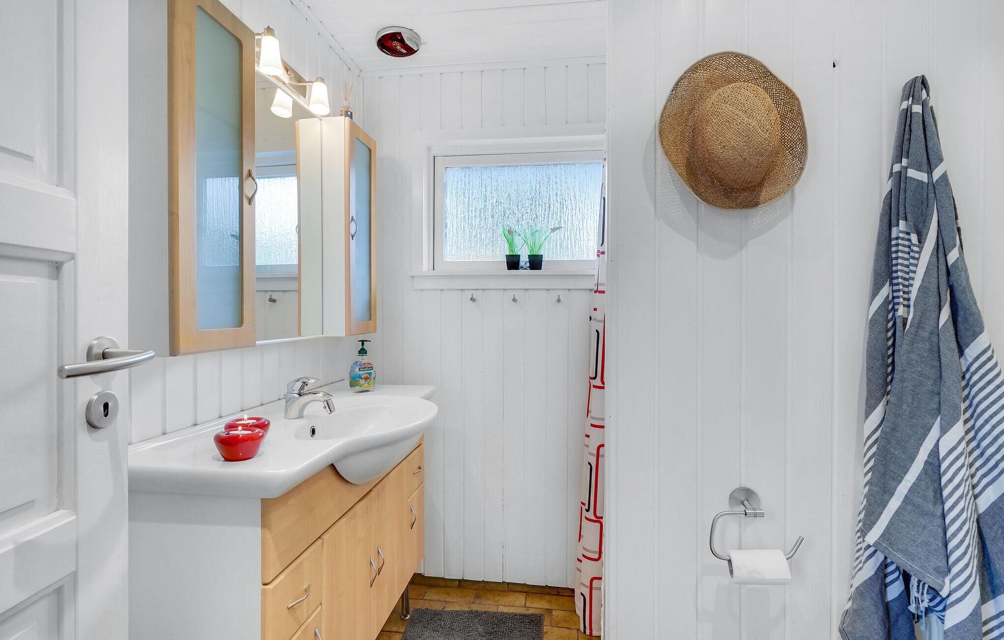 A bathroom with a white sink, wooden cabinets, a mirror, a window with plants, a towel rack, and a toilet paper holder.