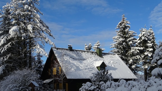 Una cabana de fusta amb un teulat inclinat, envoltada d'arbres coberts de neu i una tanca de fusta.