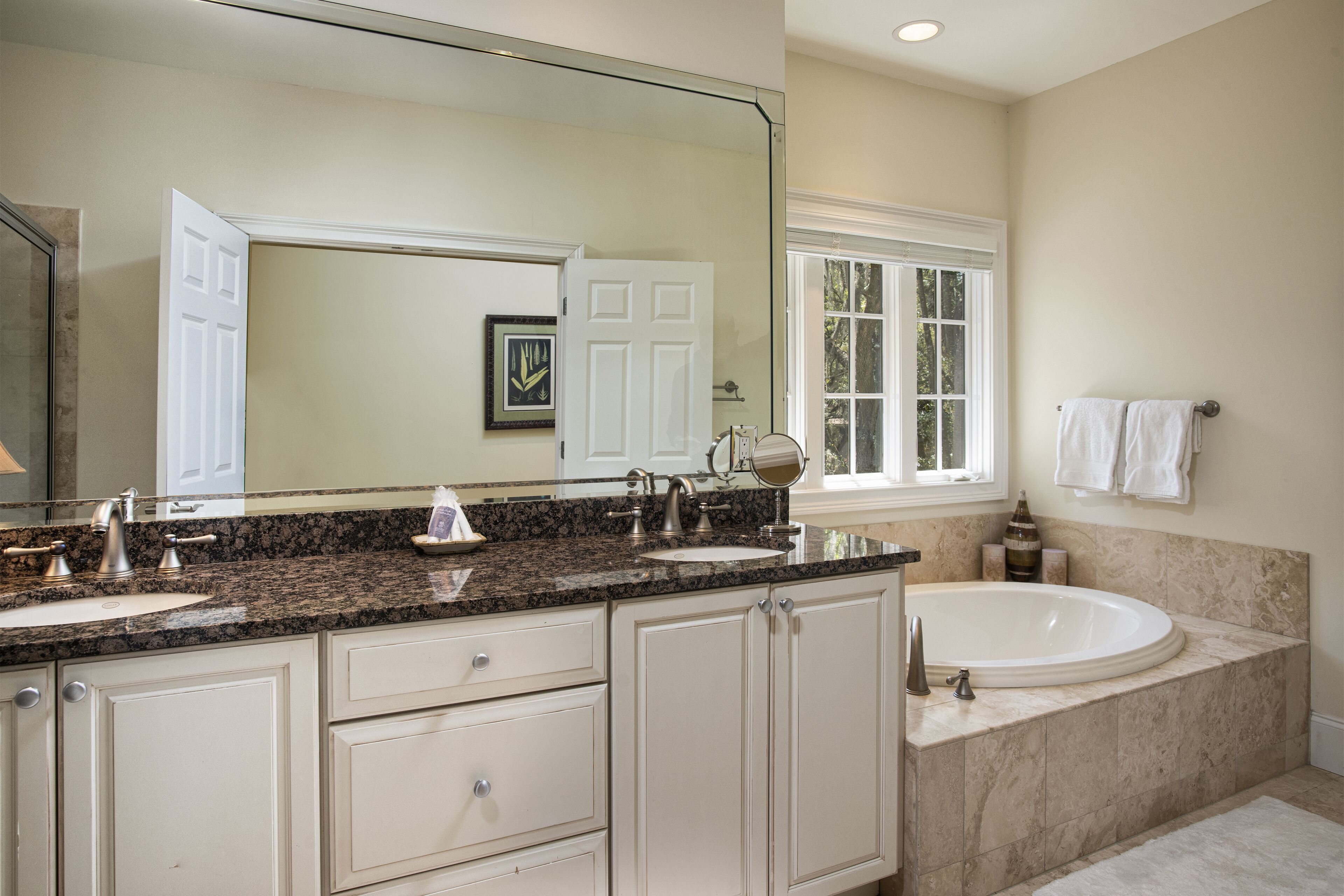 A bathroom with a large mirror, two sinks, a bathtub, and a window.