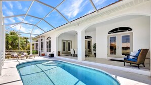 A swimming pool with a covered patio area, lounge chairs, and a wicker chair.