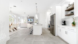 A modern kitchen with white cabinetry, a central island, stainless steel appliances, and a dining area with white furniture.