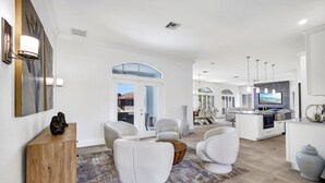 A spacious living area with a modern kitchen, white furniture, and a large window providing natural light.
