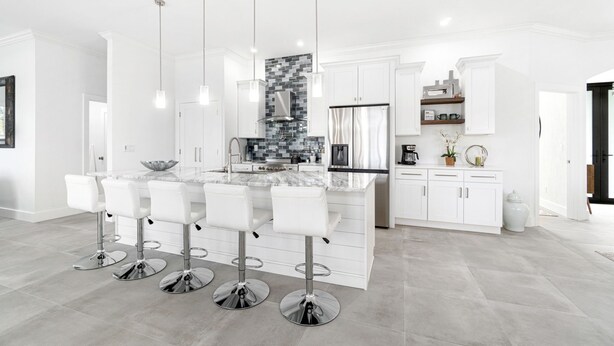 A modern kitchen with white cabinetry, a marble island with bar stools, stainless steel appliances, and pendant lighting.