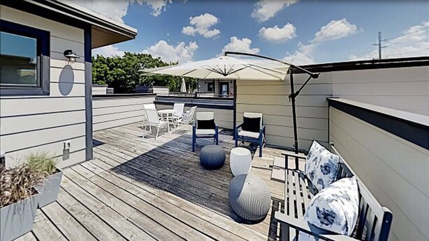 Una terraza de madera con muebles de exterior, incluyendo sillas y una mesa, bajo un paraguas grande.