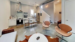 Una cocina moderna con una isla central, comedor con sillas y una escalera que lleva a otro nivel.
