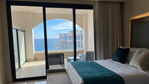 Habitación de hotel con una cama grande, vista al mar y un balcón con zona de estar.