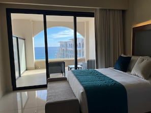 Une chambre d’hôtel avec un grand lit, une vue sur la mer et un balcon doté d’un espace salon.