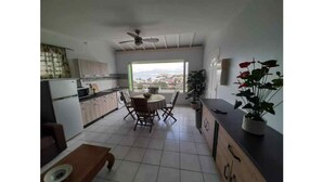 A modern kitchen with a dining area, large windows, and a ceiling fan. - L'R2 LA VILLA MELISSA T2 APARTMENT WITH POOL 150 M FROM THE BEACH. (Les Trois-Îlets)