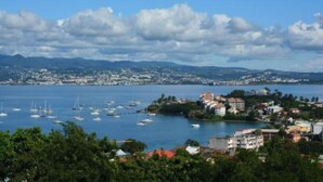 A coastal town with a marina filled with sailboats, surrounded by residential buildings and greenery. - L'R2 LA VILLA MELISSA T2 APARTMENT WITH POOL 150 M FROM THE BEACH. (Les Trois-Îlets)