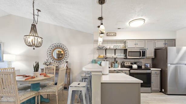 A modern kitchen with a central island, white cabinetry, stainless steel appliances, and a chandelier.