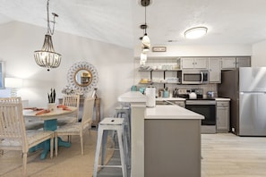 Een moderne keuken met een centraal eiland, witte kasten, roestvrijstalen apparatuur en een kroonluchter.