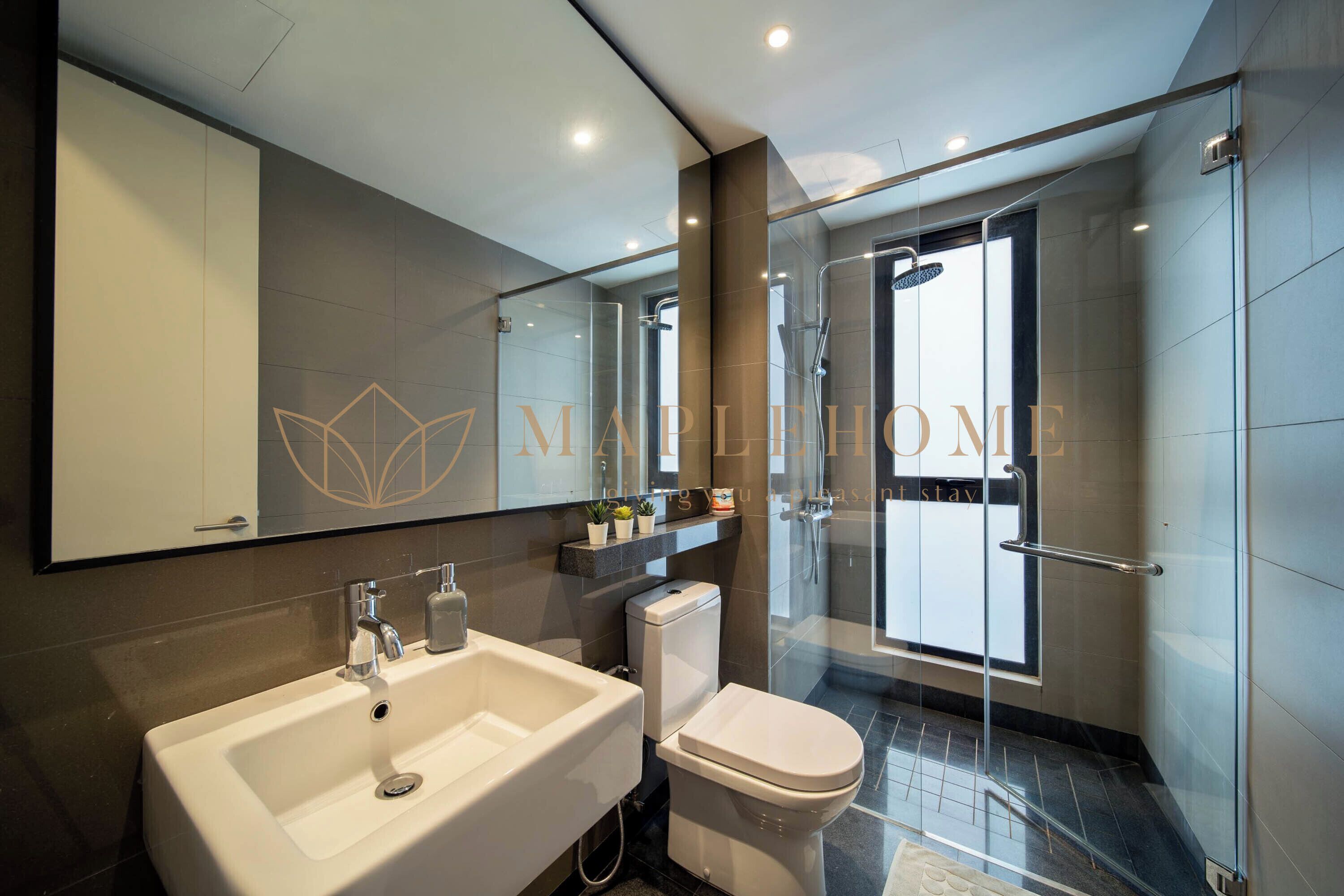 A modern bathroom with a large mirror, a sink, a toilet, and a glass shower enclosure.