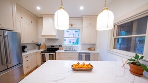 Una cocina moderna con armarios blancos, una isla de mármol y un tazón de naranjas.