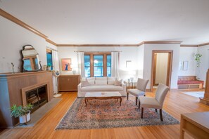 Uma sala de estar com lareira, um sofá, uma mesa de centro e uma janela grande com cortinas.