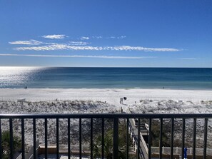 A beach view from a balcony with a wooden deck, a white fence, and sparse vegetation. - Completely renovated in Jan 2022! Free beach service! (Fort Walton Beach)