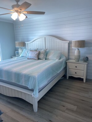 A bedroom with a white bed, striped bedding, and a ceiling fan.