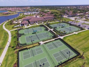Vista aérea de una zona residencial con varias canchas de tenis, un lago y casas circundantes.