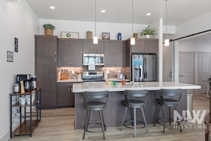 Una cocina moderna con armarios oscuros, una isla grande con taburetes de bar, electrodomésticos de acero inoxidable y una estación de café.