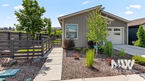 Ein modernes, eingeschossiges Haus mit Garage, umgeben von einem Holzzaun und einem angelegten Garten.