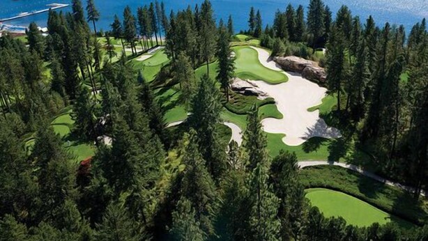 Ein Golfplatz mit Seeblick, umgeben von dichtem Wald.