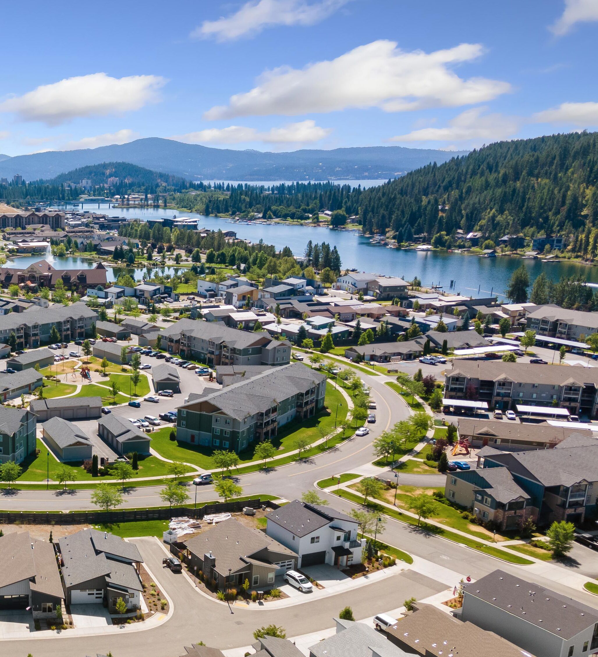 Un quartier résidentiel avec des maisons modernes, un lac et des montagnes en arrière-plan.