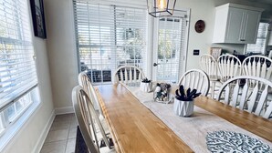 Un comedor con una mesa de madera, sillas blancas y un camino de mesa estampado.
