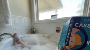 Una bañera llena de burbujas, una ventana con vistas y un libro titulado 'CASSANDRA IN REVERIE' de Holly Smaele.