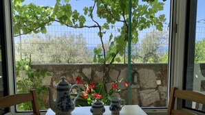 A table set with blue and white porcelain tea set, including a teapot, cups, and saucers, positioned near a window with a view of trees and a stone wall. - Apartment with sea view and pool - Orange Garden (Buljarica)