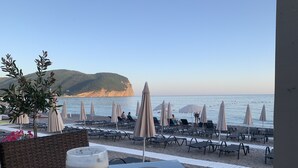 A beachside table with two glasses of beer, beach chairs, and umbrellas. - Apartment with sea view and pool - Orange Garden (Buljarica)