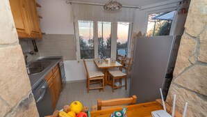 A kitchen with a dining table, chairs, a bowl of fruit, a teapot, and a refrigerator. - Apartment with sea view and pool - Orange Garden (Buljarica)