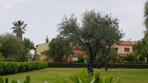 Une pelouse bien entretenue, avec un grand arbre et, au fond, un bâtiment dont le toit est recouvert de tuiles rouges.