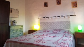 Une chambre à coucher comprenant un lit, deux tables de chevet, une commode, une armoire en bois et un mur orné de trois tableaux encadrés.