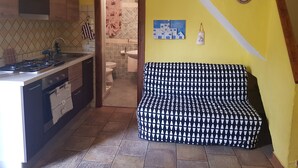 Une cuisine équipée d’une cuisinière, d’un évier et de placards, une salle de bain avec des toilettes et un lavabo, et un canapé à motifs dans une pièce aux murs jaunes.