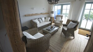 A cozy living room with wicker furniture, a wooden ceiling, and large windows with curtains. - Strandhaus-Fehmarn, port side, sea view and beach on the doorstep (Fehmarn)