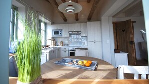A kitchen with white cabinets, a wooden ceiling, and a dining table with a tray of fruit. - Strandhaus-Fehmarn, port side, sea view and beach on the doorstep (Fehmarn)