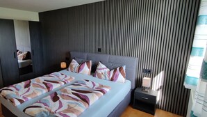 A modern bedroom with a large bed, a wardrobe, a bedside table with a lamp, and a striped wall. - 🌞FeWo Berger, quiet location on the outskirts of Frauenzell, near Center Parcs in the Allgäu (Altusried - Frauenzell)