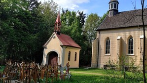 Eine Kirche mit rotem Kirchturm und Glockenturm, umgeben von einem Friedhof mit hölzernen Kreuzen.