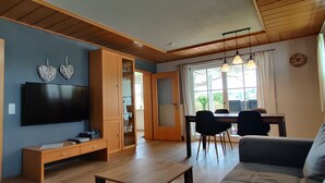 Ein Wohnzimmer mit Flachbildfernseher, Holzmöbeln und einem Essbereich mit Stühlen und Tisch.