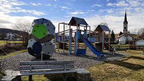 A playground with a slide and climbing structures, a church in the background, and a bench in the foreground. - 🌞FeWo Berger, quiet location on the outskirts of Frauenzell, near Center Parcs in the Allgäu (Altusried - Frauenzell)