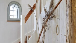 Un escalier avec des rampes blanches et des poutres en bois, menant à un palier agrémenté d’une plante en pot et d’un mur au style rustique.