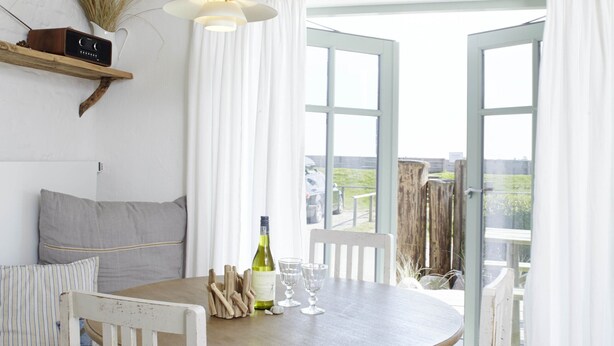 Un coin repas avec une table ronde en bois, des chaises blanches et un luminaire suspendu.