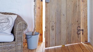 Une porte en bois rustique ornée d’une découpe en forme de cœur, un panier en osier et un seau en métal posés sur le sol.