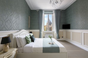 Una camera da letto con un letto, un comodino, una lampada, una TV e una finestra vista su una cupola e degli edifici.
