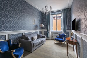 Una stanza con un divano grigio, poltrone blu, un tavolino e un lampadario.