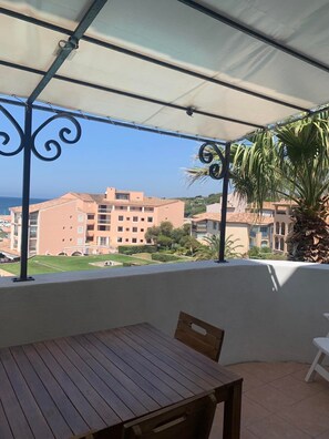 Ein überdachter Außenbereich mit Tisch und Stühlen mit Blick auf einen Wohnkomplex und das Meer.