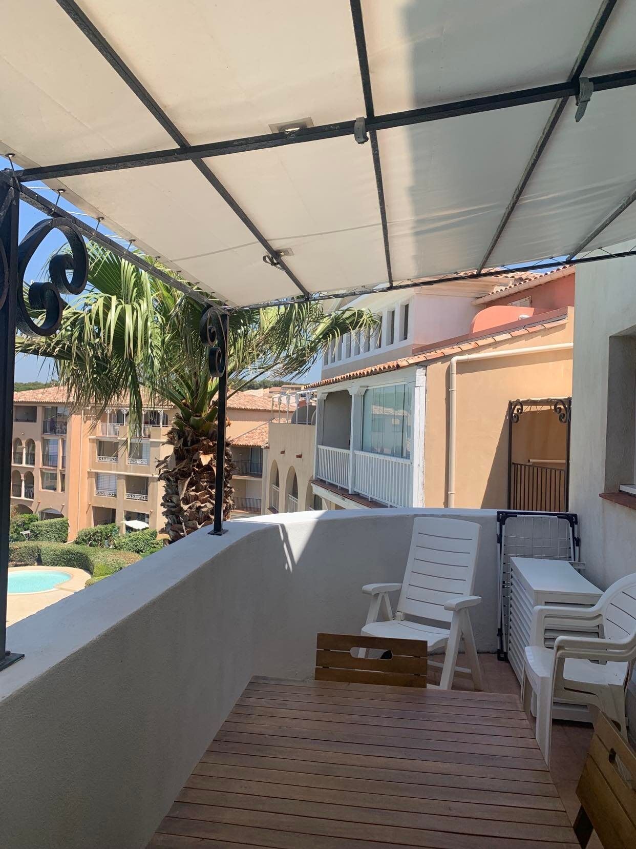 Een balkon met houten vloer, witte stoelen en een palmboom.