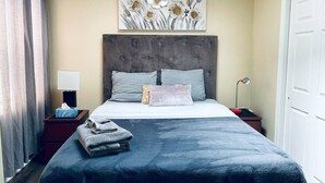 A hotel room with a bed, a nightstand, a lamp, a painting on the wall, and a door. - Cozy 1BD Apt @Magic Garden in Center City (Philadelphia)