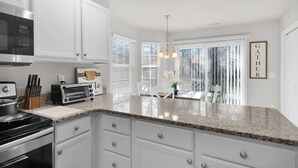 A kitchen with white cabinets, a granite countertop, a microwave, a toaster, and a hanging light fixture. - Stylish Luxe One-Level Twnh Steps from Neuse Trail (Raleigh)