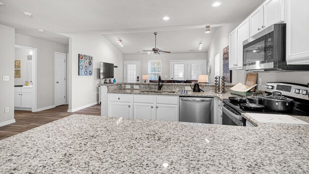 A spacious kitchen with granite countertops, white cabinetry, a central island, and a built-in oven. - Stylish Luxe One-Level Twnh Steps from Neuse Trail (Raleigh)