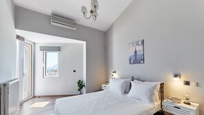 Une chambre avec un grand lit, des tables de chevet, une commode, une fenêtre avec des rideaux, un climatiseur fixé au mur et une affiche représentant un paysage urbain.